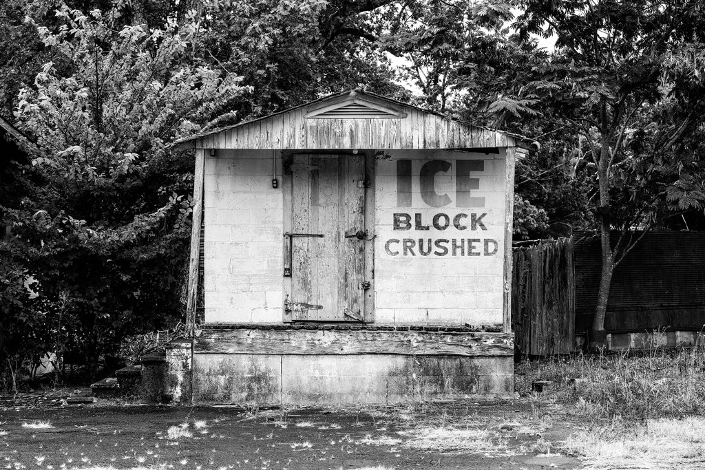 Black and white photograph of an abandoned ice block house with the words "Ice Block Crushed" painted on its front facade.