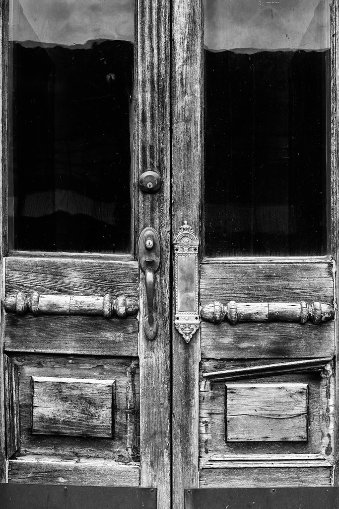 Black and white photograph of a two weathered and aged antique doors on a vacant storefront in a small town.