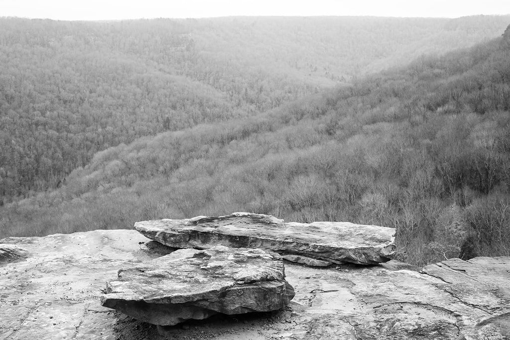 Black and white landscape photograph of a mountain vista seen from a rocky overlook.