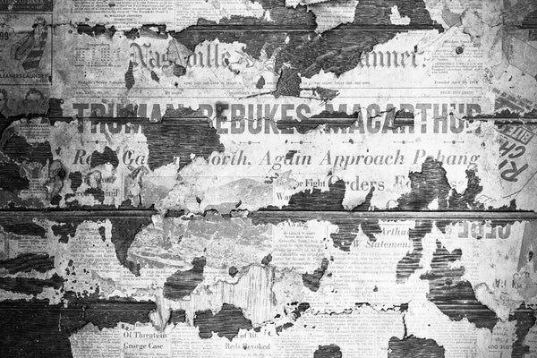 Black and white photograph of a 1951 Nashville Banner newspaper pasted on the interior walls of an abandoned old farmhouse. The boldface headline says "Truman Rebukes MacArthur." The Nashville Banner was published from 1876 until 1998.