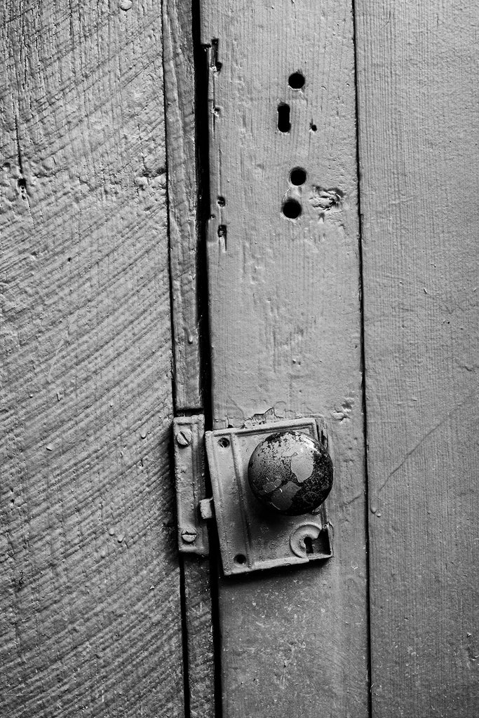 Black and white detail photograph of a rustic old wooden door with an antique door knob.