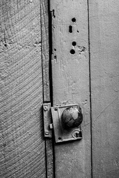 Black and white detail photograph of a rustic old wooden door with an antique door knob.