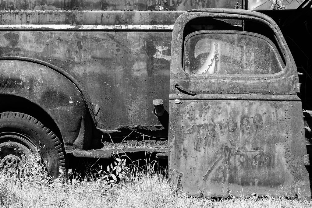 Black and white photograph of a beautifully rusting antique work truck abandoned in the grass