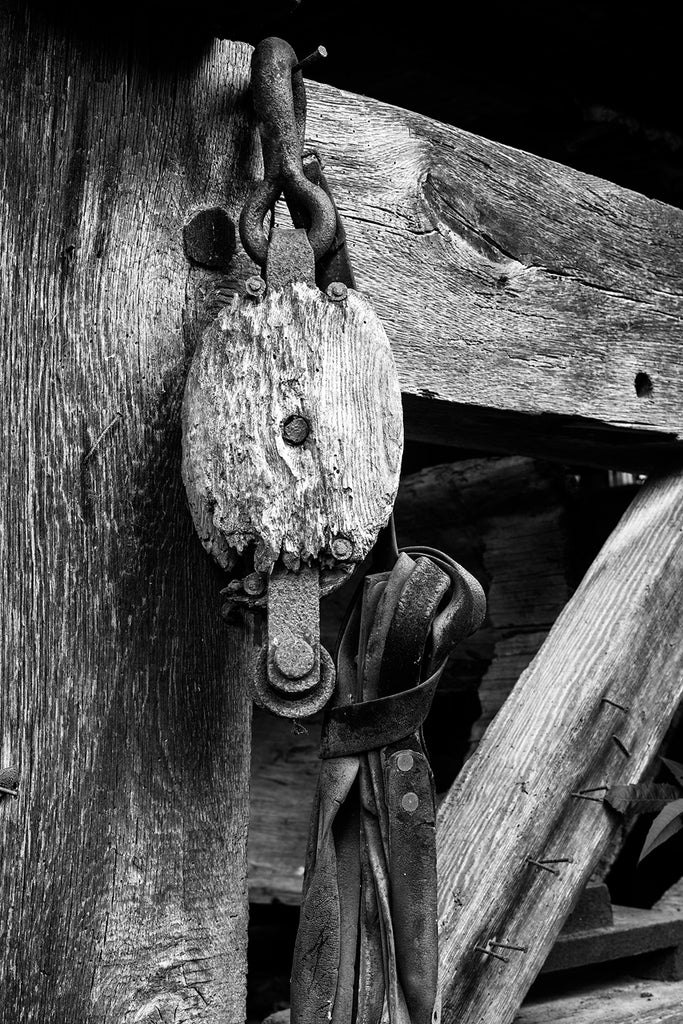 Black and white photograph of weathered old farm equipment made of iron, wood, and leather.