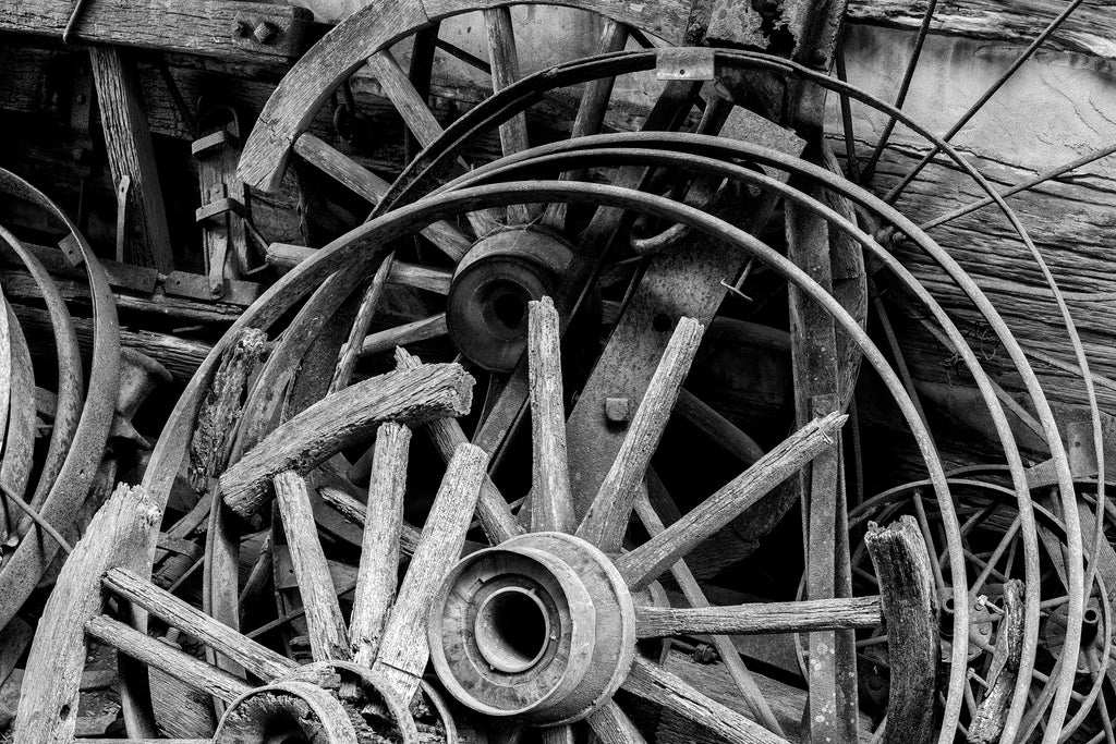 Black and white photograph of a jumble of old wooden wagon wheels with broken spokes and rims found on an old farm.