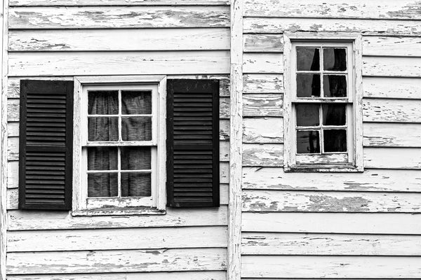 Black and white photograph of two windows on an old house with peeling paint and crooked walls found in Charleston.