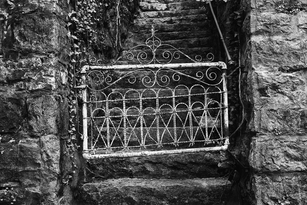 Black and white photograph of a small, white, antique gate as seen in a small town.