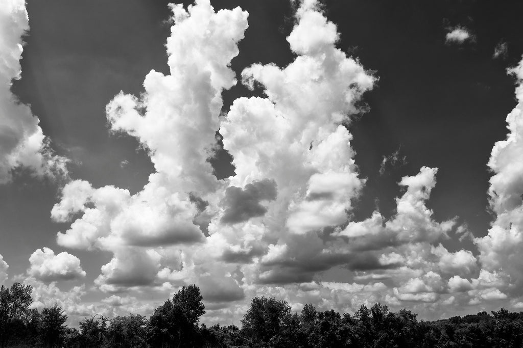 Black and white landscape photograph featuring massive clouds across a blue summer sky.