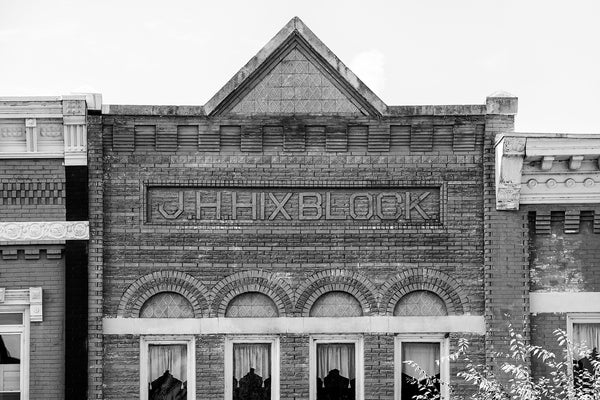 Black and white architectural photograph of brick details on a historic small town storefront that reads JH Hix Block. Mr. Hix opened what was described as a "bar and confectioner" business in 1880.