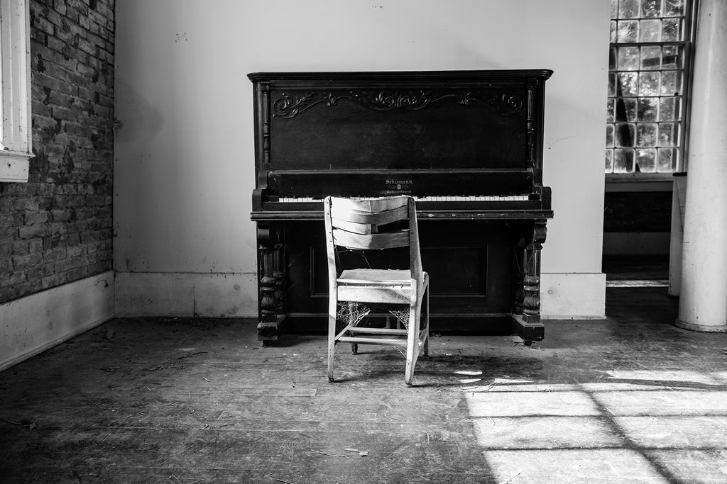 Black and white photograph of a dusty piano inside an abandoned church.