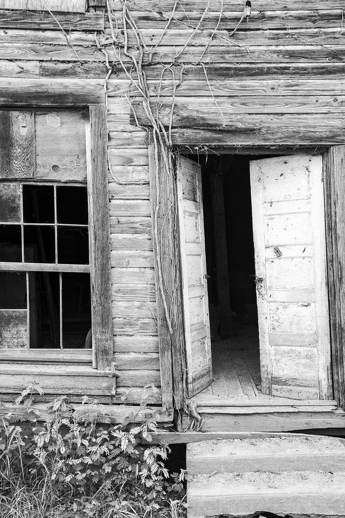 Black and white photograph of the front of a crooked, old, wooden building found in in a ghost town. 