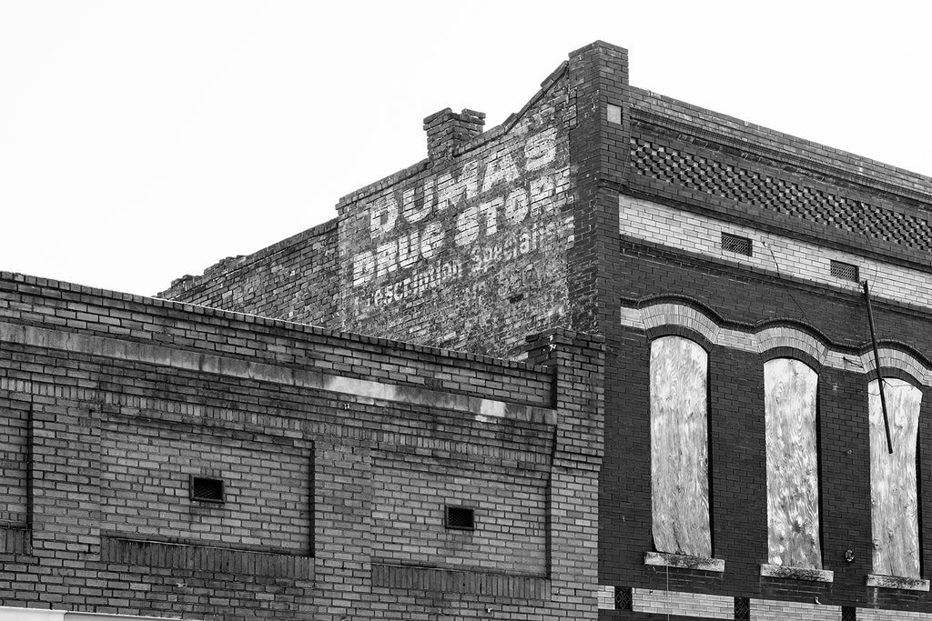 Black and white photograph of a fading old painted sign for Dumas Drug Store atop an abandoned building in downtown Natchez Mississippi