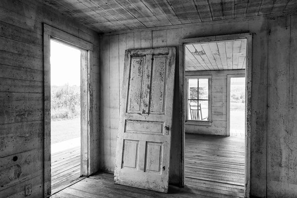 Black and white photograph of an old door leaning against the wall inside an abandoned farm house.