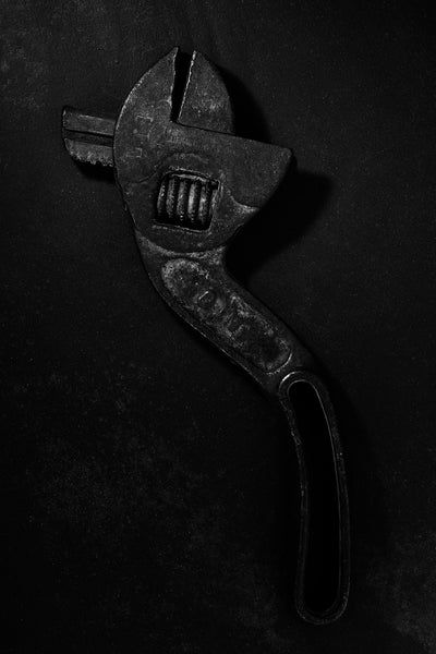 Dramatic black and white photograph of an antique S-shaped Westcott wrench in extremely low light.