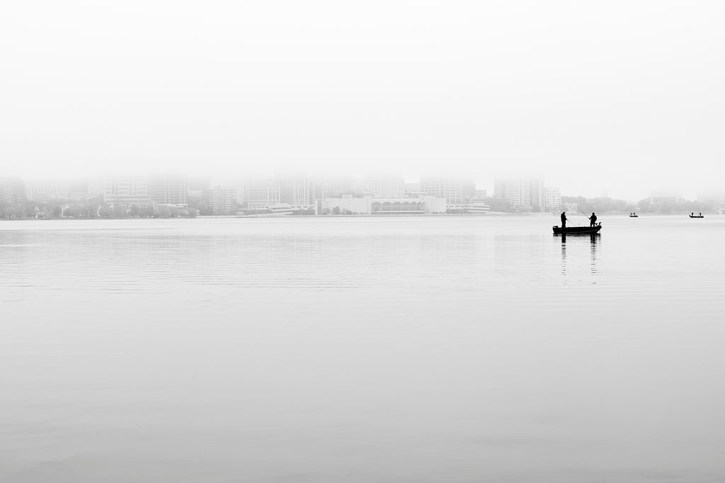 Black and white photograph of fishermen on a boat on Lake Monona with the foggy city skyline of Madison, Wisconsin shrouded in white along the horizon