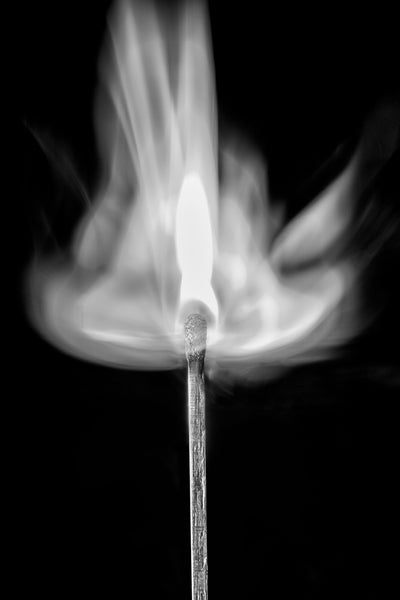 Minimalist black and white photograph of a wooden match at the exact instant of ignition.