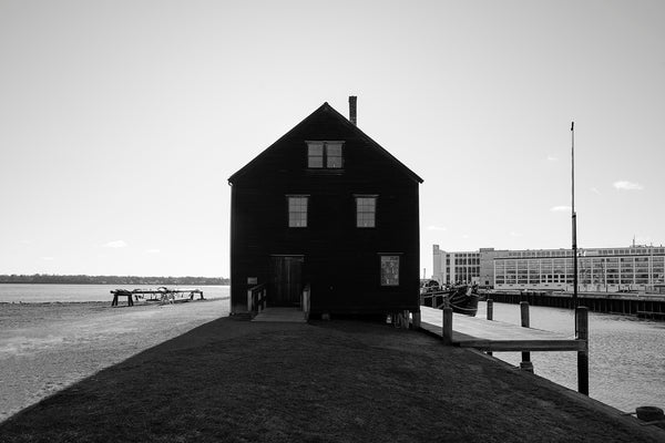 Black and white photograph of the historic old sail loft building in near silhouette as the morning sun rises behind it along the Massachusetts coast in Salem.