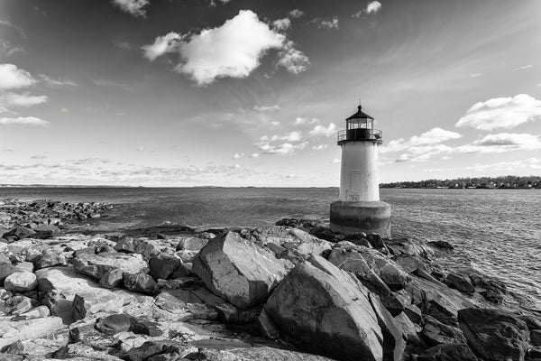 Black and white photograph of the rocky New England coast with ocean, clouds, and a small lighthouse.