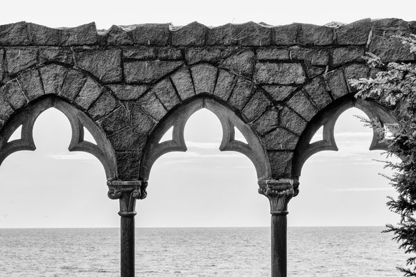 Black and white photograph of three stone arches outside an old mansion overlooking the ocean.