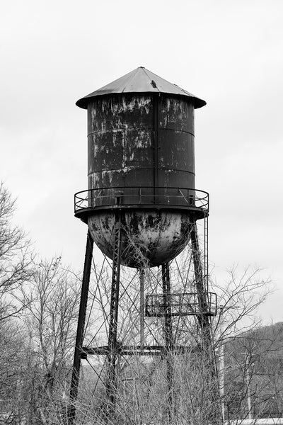 Black and white photograph of a rusty steel water tower among trees on the property of an old southern textile mill.