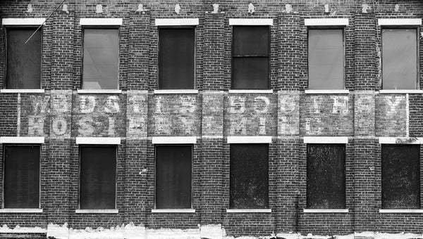Black and white photograph of a faded multiple-layer old sign on the brick wall of an old southern textile mill. The W.B. Davis Hosiery Mill operated from 1884-1974 in Ft. Payne, Alabama.