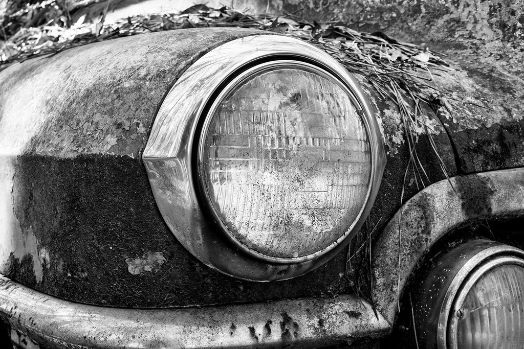 Black and white photograph of the headlight of a rusty antique automobile. 