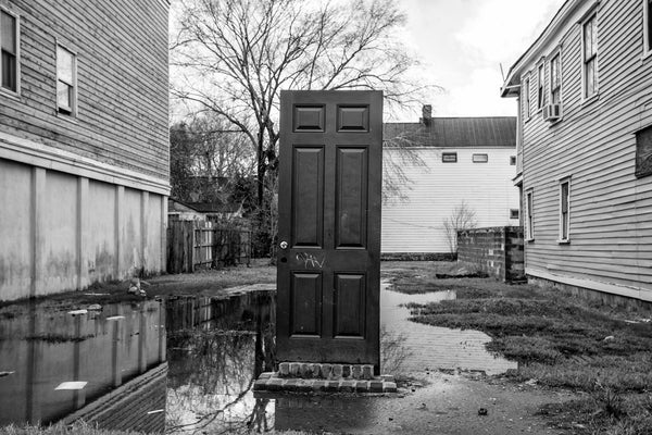 Black and white photograph of a standing front door without a house attached, seen in an empty lot in Charleston, South Carolina.