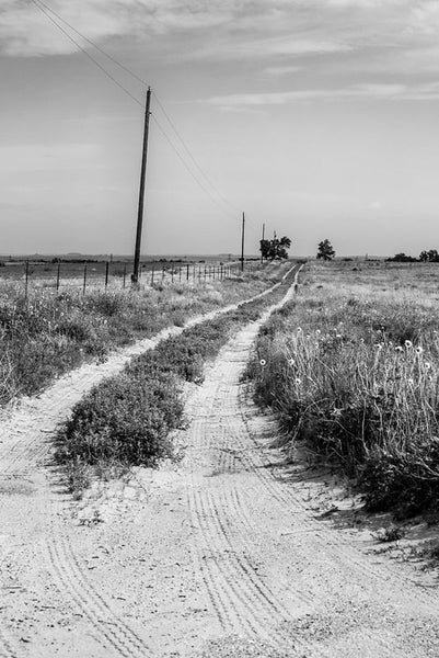 Black and white photograph of a dirt road leading into the flat, wide horizon of the Texas Panhandle.