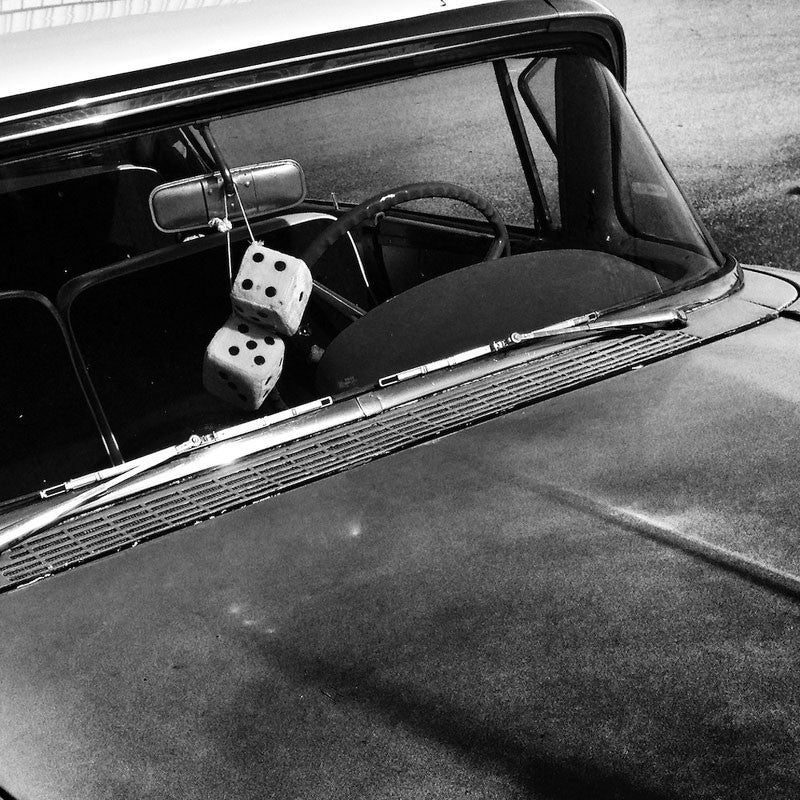 Black and white Instagram photograph of fuzzy dice on the rear view mirror of a restored 1950s automobile.