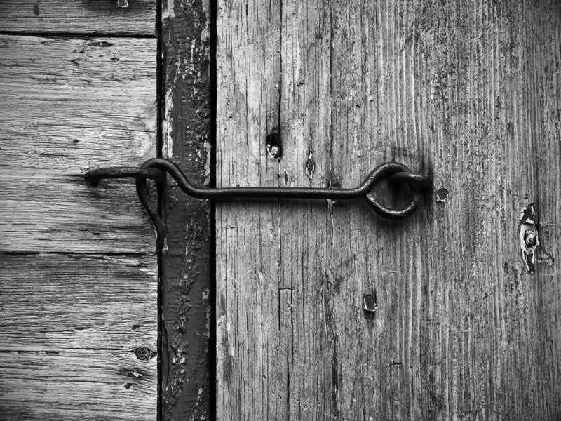 Black and white detail photograph of a door latch on the screen door of an old house.