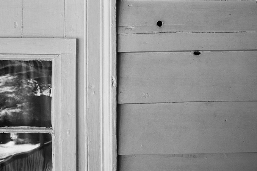 Black and white photograph of the exterior back porch of the historic Carter House in Franklin, Tennessee, with original bullet holes from the battle of Franklin still visible in the siding.