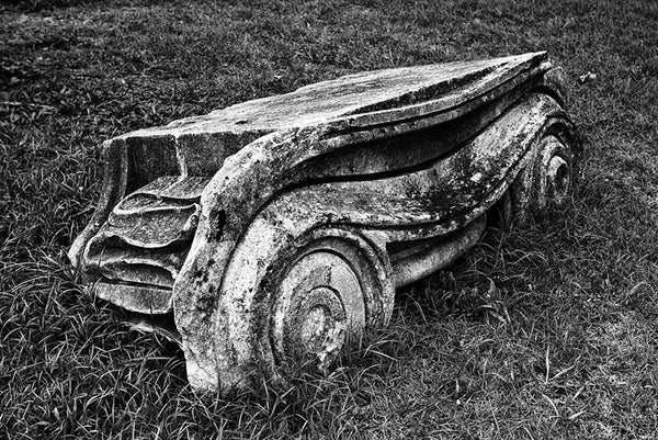 Black and white photograph of an Ionic Capitol from a Greek Revival column lying in the grass. Removed from the original Tennessee State Capitol building in Nashville during a renovation, these pieces of stone columns have been scattered around Nashville as a reminder of its reputation as "the Athens of the South."