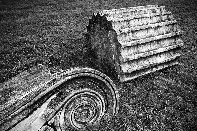 Black and white photograph of a fallen Greek Revival column lying in the grass. Removed from the original Tennessee State Capitol building in Nashville during a renovation, these pieces of stone columns have been scattered around Nashville as a reminder of its reputation as "the Athens of the South."