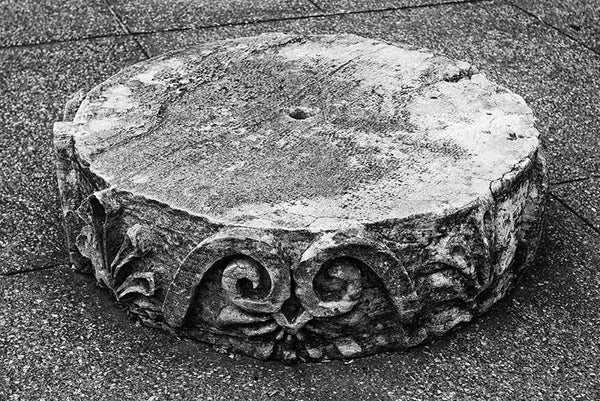 Black and white photograph of a disk section from a Greek Revival column lying on the ground. Removed from the original Tennessee State Capitol building in Nashville during a renovation, these pieces of stone columns have been scattered around Nashville as a reminder of its reputation as "the Athens of the South."