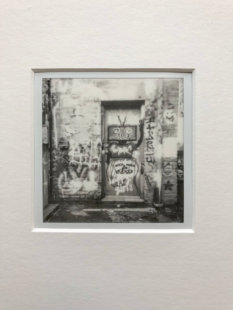 Original one-of-a-kind Polaroid photograph of graffiti in an alley, featuring a robot among other things. Archivally mounted and over-matted with white 4-ply mat. Ready to fit an 11″ x 14″ frame.