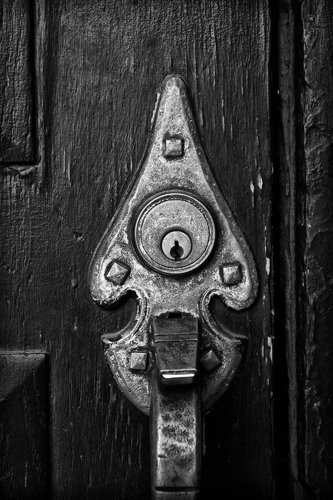 Black and white architectural detail photograph of an old brass door handle on a textured black door.