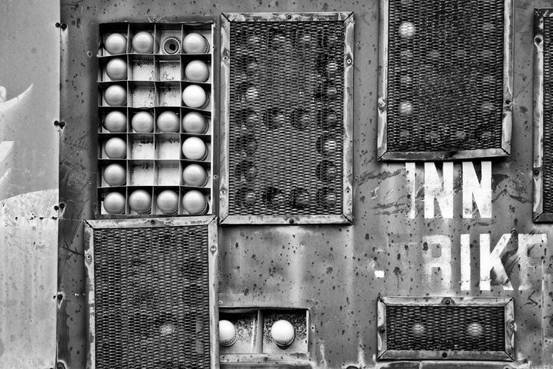 Black and white photograph of a section of an old, fading and dented scoreboard on the outfield of an abandoned baseball field. The ball field has since been plowed under and converted to parkland, and the scoreboard has been scrapped.