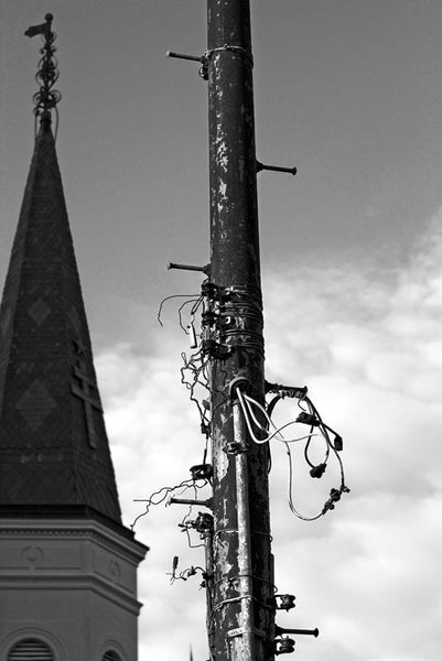 Black and white photograph of an unkempt utility pole in New Orleans' Jackson Square. One of the spires of St. Louis Cathedral is visible on the left.