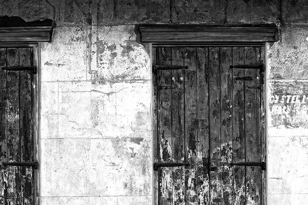 Black and white photograph of a beautifully textured wall with wooden window shutters and fading paint, seen in the New Orleans French Quarter.