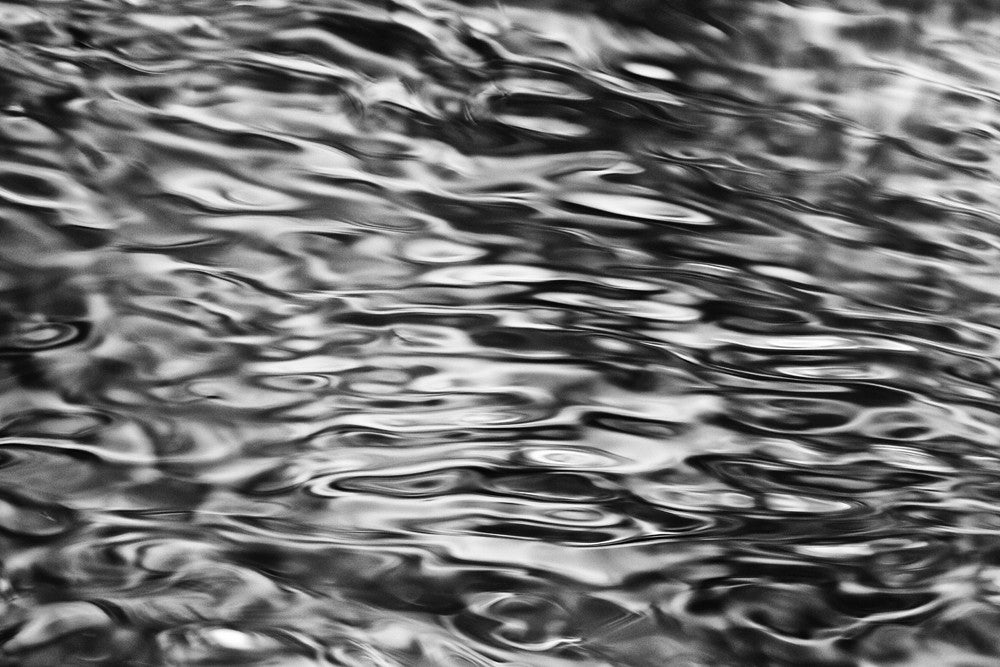 Black and white photograph of the calm, languid movement of ripples in a running river.