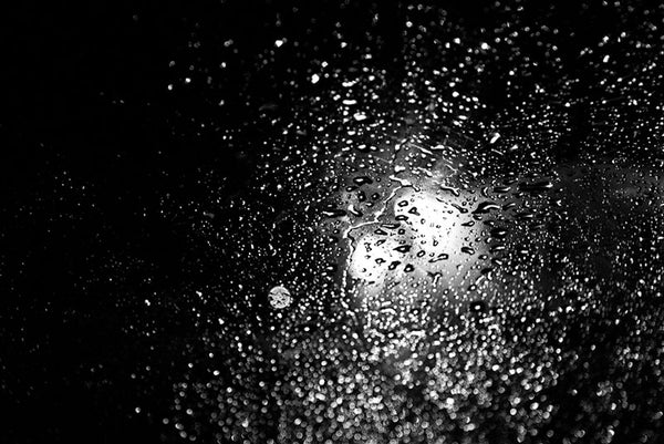 Black and white photograph of car headlights shining through a rainy car window at night.