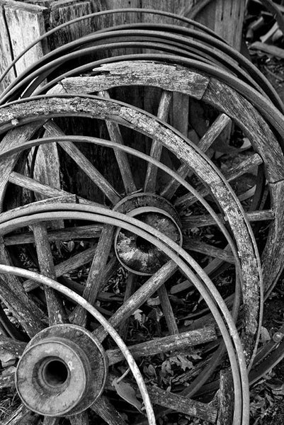 Black and white photograph of a stack of broken old wooden wagon wheels and metal rims.