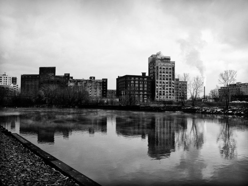 Black and white photograph of industrial buildings reflecting in a river in Milwaukee.