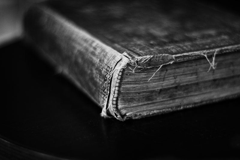 Black and white photographic study of a tattered old history book from 1904 lying on a black table.