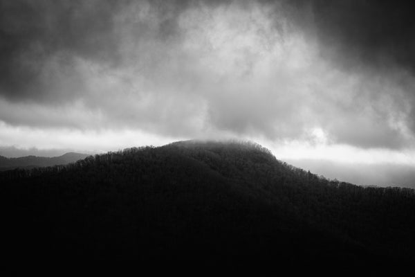 Dramatic black and white landscape photograph of tumultuous low-hanging clouds brushing across the peak of an ancient mountain in the Eastern U.S.
