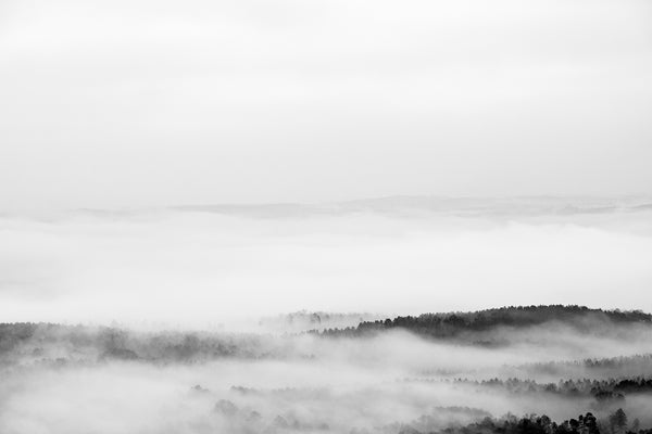 Black and white landscape photograph showing only the highest hilltops visible above valley filled with dense drifting fog.