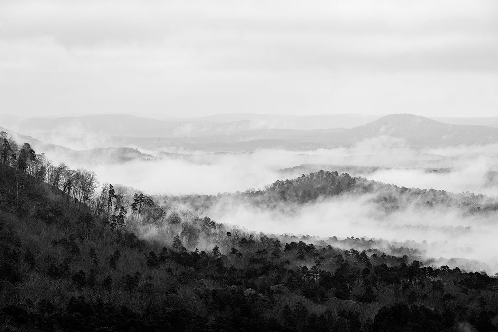 Black and white photograph of a valley filled with morning fog leaving only the mountain peaks visible above the rapidly rising mists.