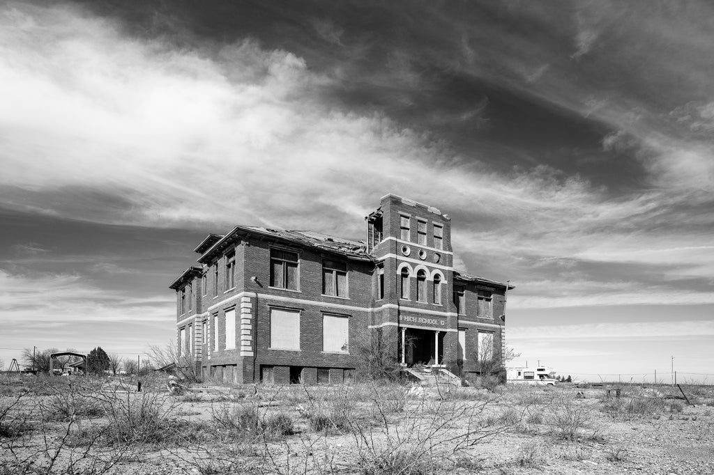 Black and white photograph of a desert landscape featuring an abandoned and derelict high school building.