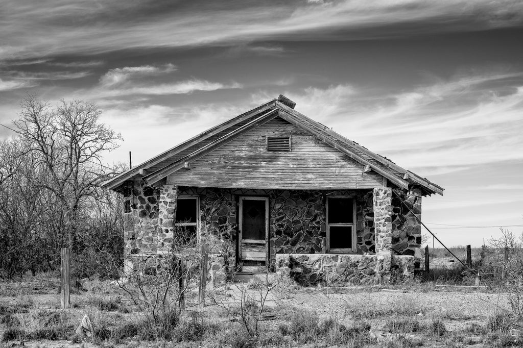 Black and white photograph of an abandoned old stone house on the edge of a small town in the desert.