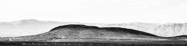Black and white wide panoramic landscape photograph of rugged western desert mountains.